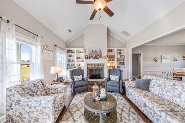 living room with visible vents, a wainscoted wall, wood finished floors, a stone fireplace, and lofted ceiling