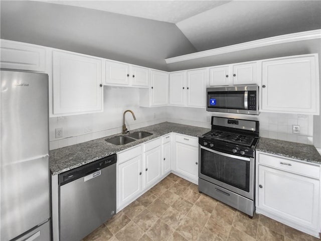 kitchen with lofted ceiling, stainless steel appliances, a sink, white cabinets, and dark stone counters