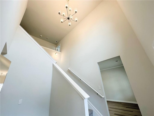 stairs with an inviting chandelier, baseboards, a towering ceiling, and wood finished floors