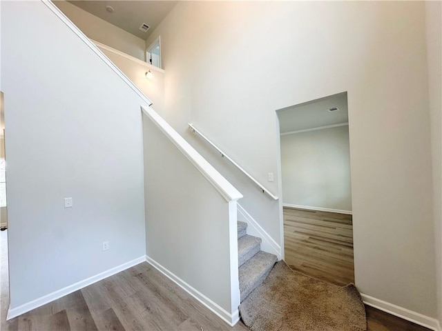 staircase featuring a towering ceiling, baseboards, and wood finished floors