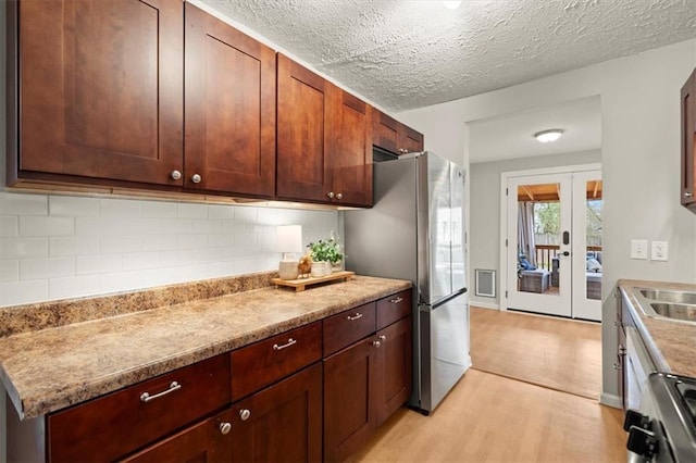 kitchen with french doors, a textured ceiling, light hardwood / wood-style flooring, stainless steel refrigerator, and backsplash