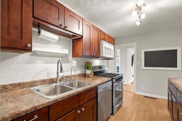 kitchen featuring sink, tasteful backsplash, a textured ceiling, light wood-type flooring, and stainless steel appliances