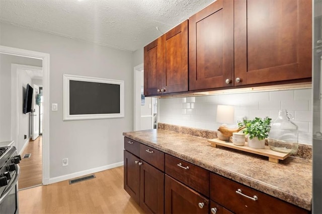 kitchen featuring light stone counters, light hardwood / wood-style floors, stainless steel stove, and backsplash