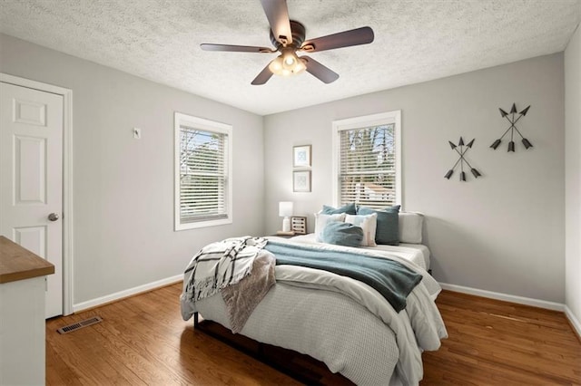 bedroom with multiple windows, ceiling fan, hardwood / wood-style flooring, and a textured ceiling