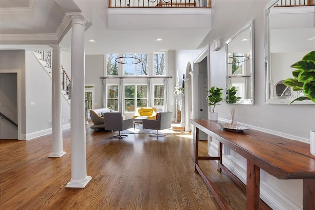 foyer entrance with crown molding, stairway, a towering ceiling, wood finished floors, and ornate columns