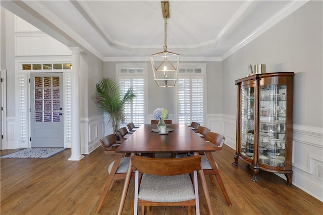 dining area featuring decorative columns, a raised ceiling, wood finished floors, and a decorative wall