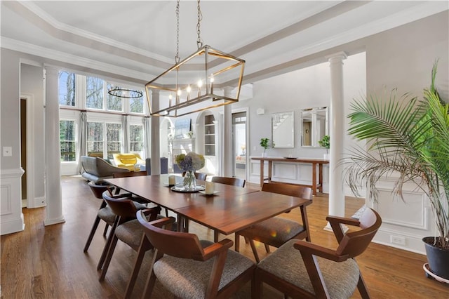 dining area with a tray ceiling, decorative columns, wood finished floors, and ornamental molding