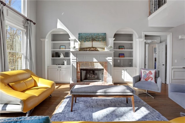 living area featuring built in features, a fireplace, a high ceiling, and wood finished floors