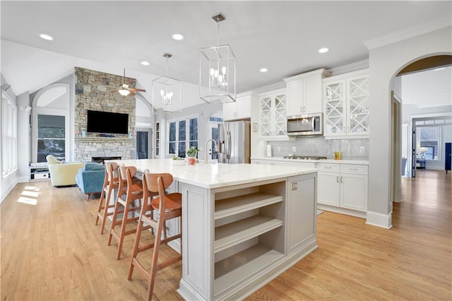 kitchen featuring open shelves, stainless steel appliances, a stone fireplace, white cabinets, and vaulted ceiling