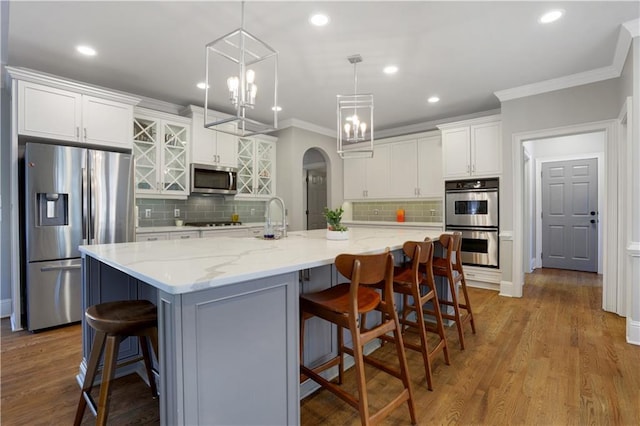 kitchen with wood finished floors, arched walkways, stainless steel appliances, white cabinetry, and crown molding