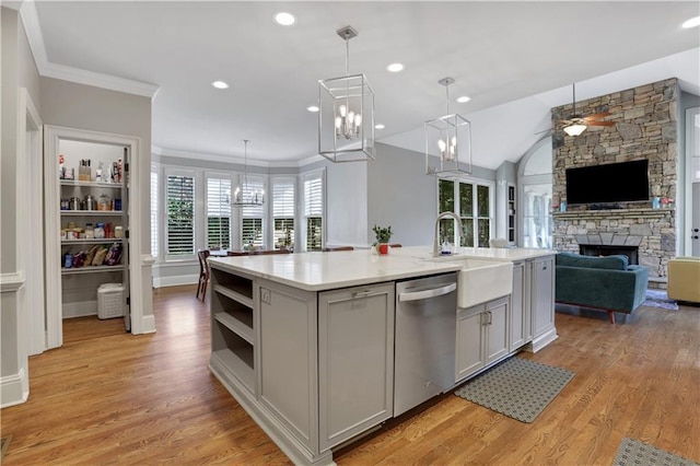 kitchen with a sink, open floor plan, a stone fireplace, light countertops, and dishwasher