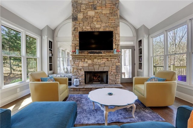 living room featuring built in features, wood finished floors, baseboards, a stone fireplace, and vaulted ceiling