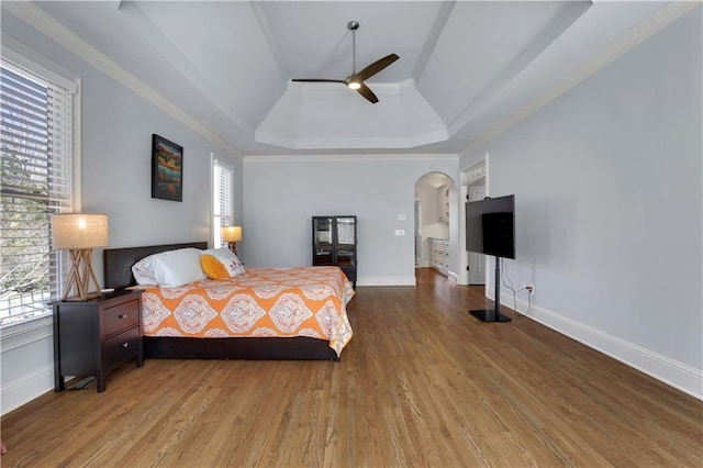 bedroom with a raised ceiling, wood finished floors, arched walkways, and baseboards