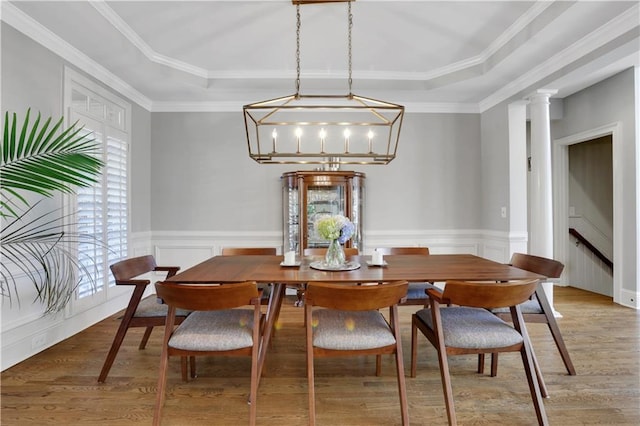 dining room featuring light wood finished floors, wainscoting, a raised ceiling, and ornate columns