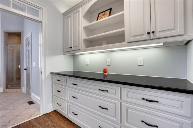 kitchen with wood finished floors, baseboards, open shelves, white cabinetry, and dark countertops