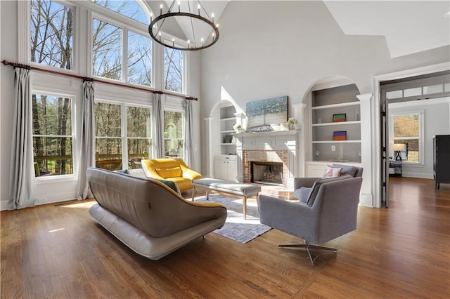 living room with built in features, wood finished floors, an inviting chandelier, and a fireplace with raised hearth