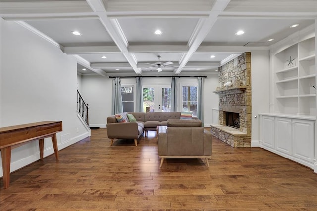 living area featuring coffered ceiling, wood finished floors, stairway, a stone fireplace, and baseboards