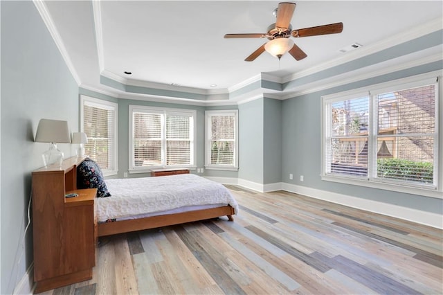 bedroom with a tray ceiling, light wood-style flooring, multiple windows, and baseboards