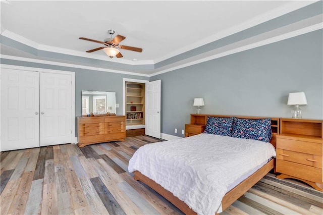 bedroom featuring a raised ceiling, wood finished floors, a closet, and ornamental molding