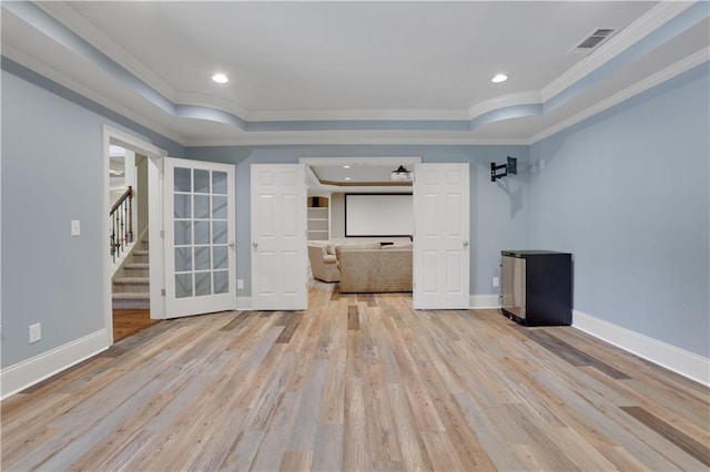 empty room featuring stairs, a raised ceiling, light wood-style floors, and visible vents