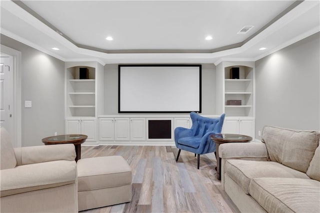 cinema with built in features, a tray ceiling, and light wood-style floors