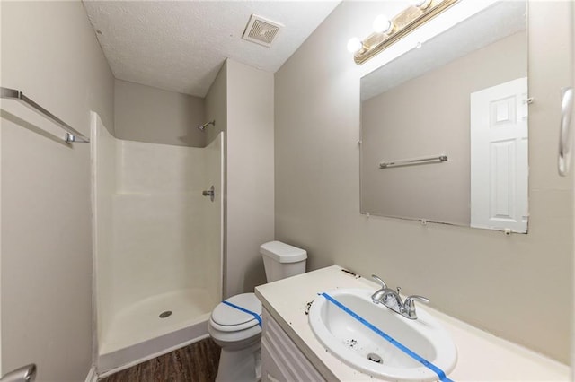 bathroom featuring wood-type flooring, a shower, a textured ceiling, toilet, and vanity