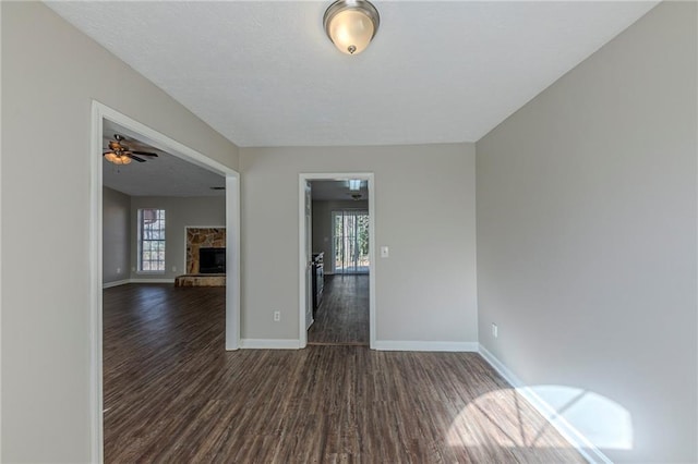 unfurnished room with ceiling fan, dark wood-type flooring, and a stone fireplace