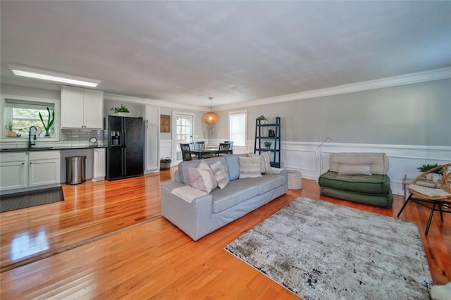 living room with ornamental molding, sink, and light wood-type flooring