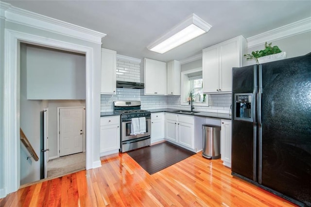 kitchen with sink, crown molding, stainless steel gas stove, white cabinetry, and black refrigerator with ice dispenser