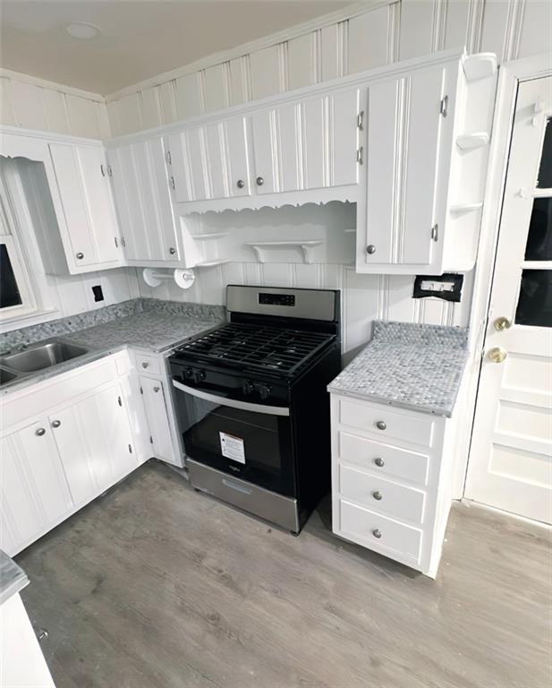 kitchen featuring white cabinetry, sink, stainless steel gas range, light stone counters, and light hardwood / wood-style flooring