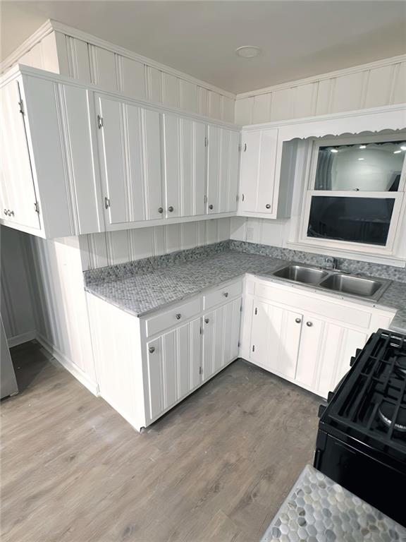 kitchen featuring white cabinetry, sink, black range, and light wood-type flooring