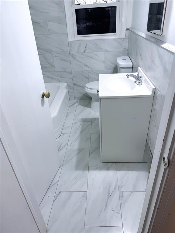 bathroom with a tub to relax in, vanity, tile walls, and toilet