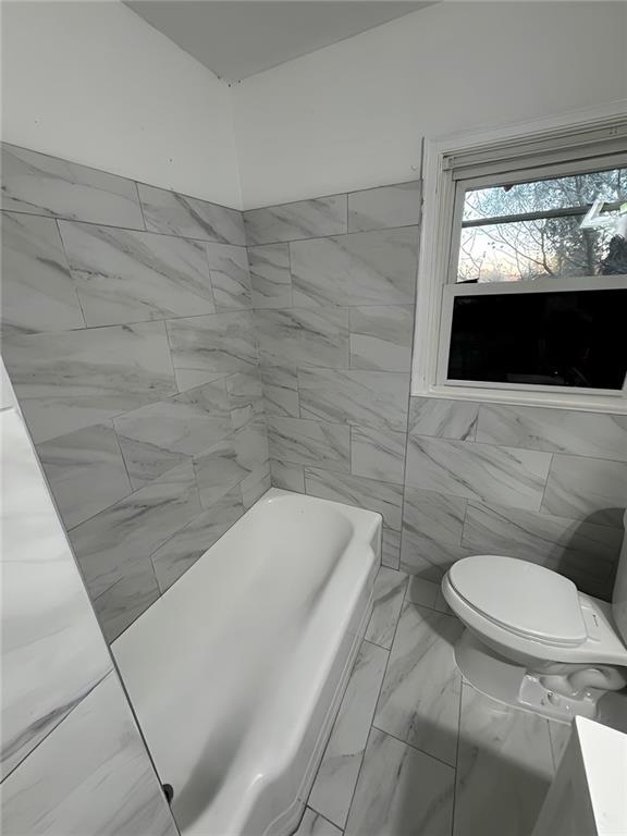 bathroom featuring a tub to relax in, toilet, and tile walls