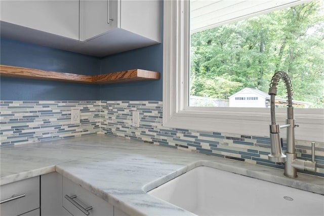 room details featuring open shelves, decorative backsplash, light stone countertops, white cabinets, and a sink