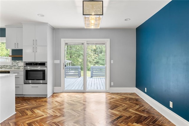 kitchen featuring oven, baseboards, light countertops, white cabinetry, and tasteful backsplash