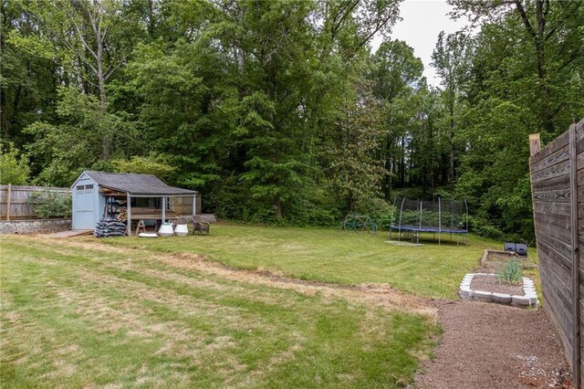 view of yard with a storage shed, fence, a trampoline, and an outbuilding