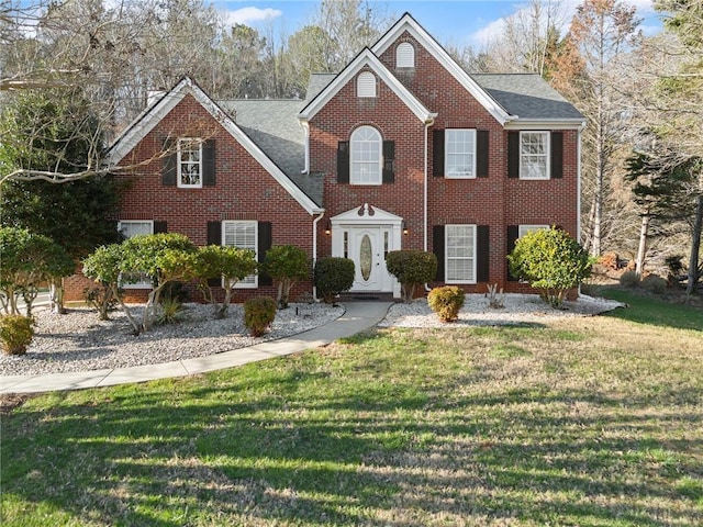 colonial house featuring brick siding, a front yard, and roof with shingles