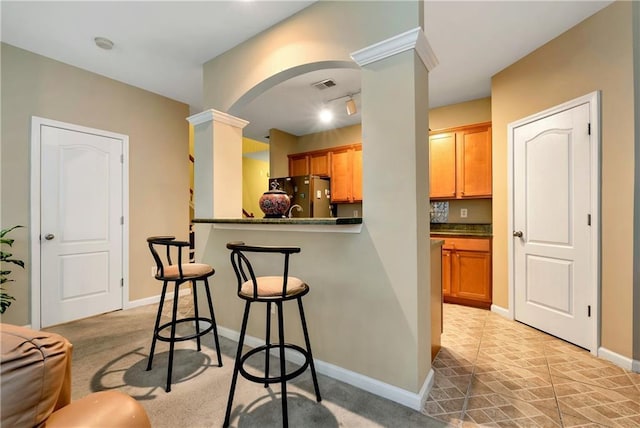 kitchen with light carpet, kitchen peninsula, stainless steel refrigerator, and ornate columns