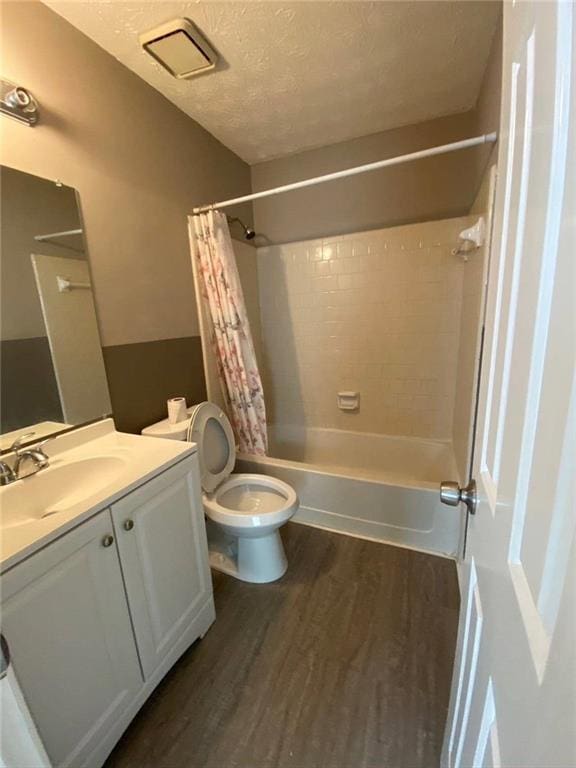 bathroom featuring vanity, a textured ceiling, toilet, shower / bath combo with shower curtain, and wood finished floors