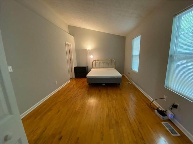 bedroom with lofted ceiling, visible vents, baseboards, and wood finished floors