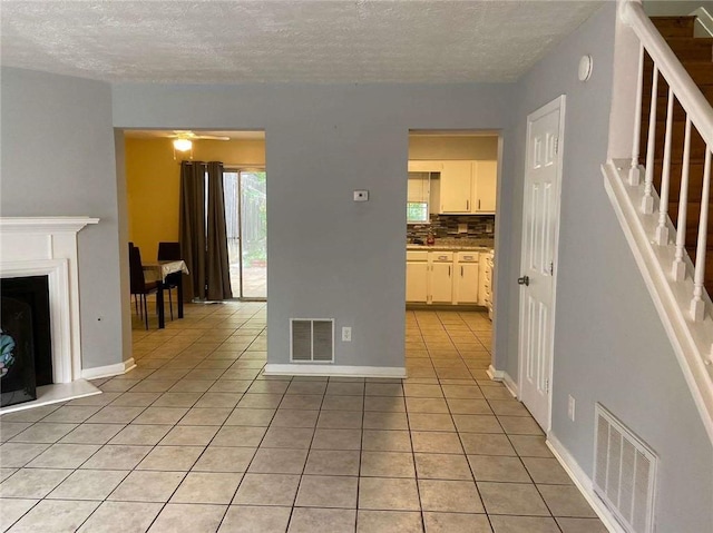 unfurnished living room featuring a textured ceiling, light tile patterned flooring, visible vents, and stairway