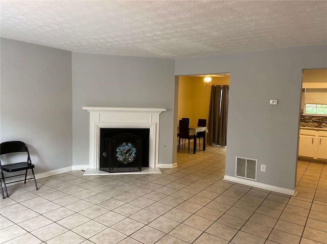 unfurnished living room featuring light tile patterned floors, visible vents, a textured ceiling, and baseboards