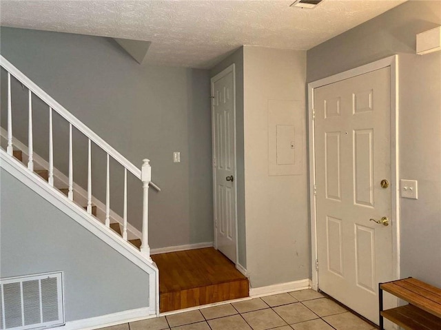 tiled entryway with stairway, visible vents, a textured ceiling, and baseboards