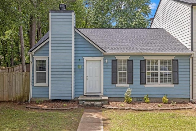 view of front facade featuring a chimney, a front yard, roof with shingles, and fence
