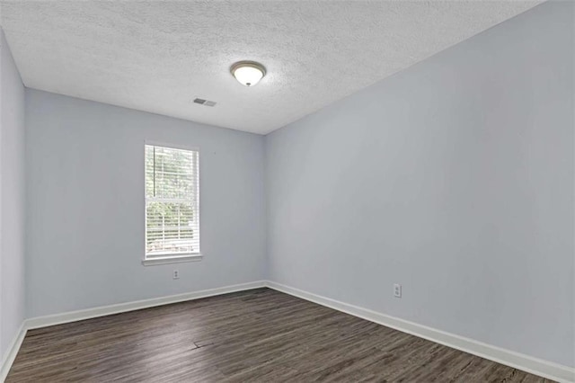 spare room featuring a textured ceiling, dark wood-type flooring, baseboards, and visible vents