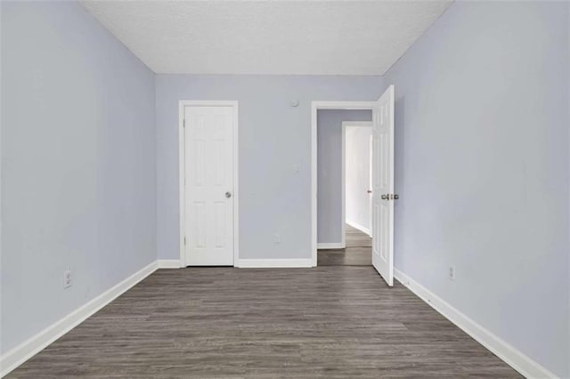 unfurnished bedroom with a textured ceiling, baseboards, and dark wood-style floors