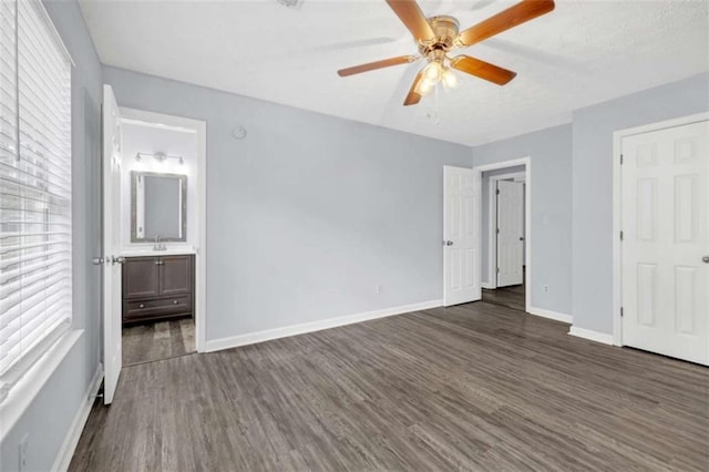 unfurnished bedroom with dark wood finished floors, ensuite bathroom, baseboards, and a sink