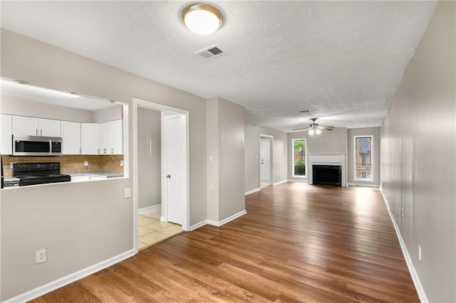2340 Beaver Ruin Rd Unit 68, Norcross, GA 30071 - unfurnished living room featuring a textured ceiling, light wood-style flooring, a ceiling fan, baseboards, and a fireplace