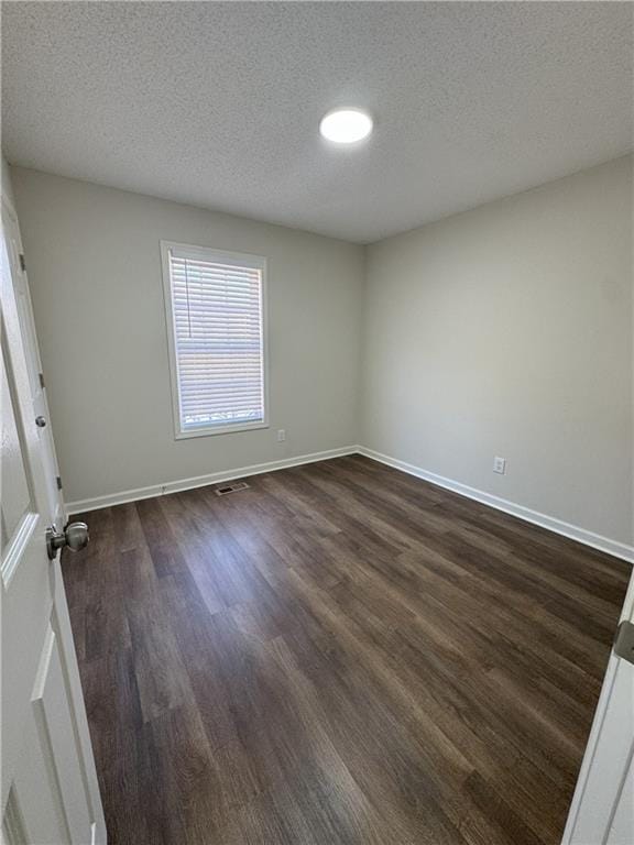 spare room with dark wood finished floors, a textured ceiling, and baseboards