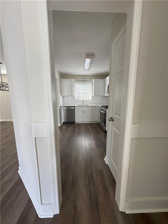 hallway with a textured ceiling, dark wood-style floors, baseboards, and a sink